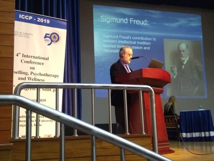 Dr. Smith presenting at a podium beside a slide about Sigmund Freud at an international conference