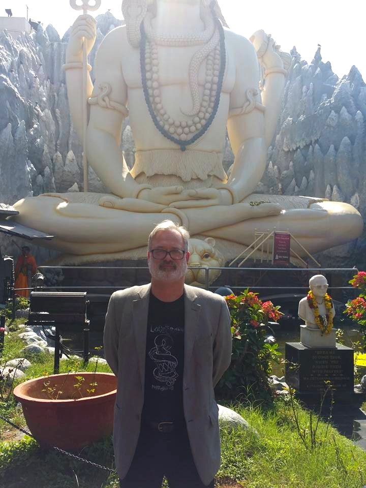 Dr. David P. Smith standing before a large white statue of a seated, meditating Shiva on a trip in India